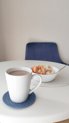 a bowl of oat meal and cup of coffee with milk on the white table in the morning