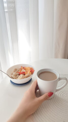 a bowl of oat meal and cup of coffee with milk on the white table in the morning