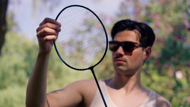 outdoors in a park with trees young brunette boy standing with a bambinton racket trying to tighten the strings on the racket
