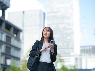 Fototapeta premium スマホを持って街を歩く女性ビジネスパーソン