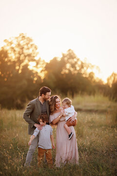 Family of four enjoying a golden sunset in a grassy field, inter