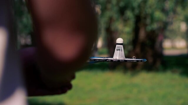 close up outdoors in a park with trees young handsome brunette guy in jeans and a white T-shirt, a brunette stuffing a shuttlecock warming up before playing bambinton