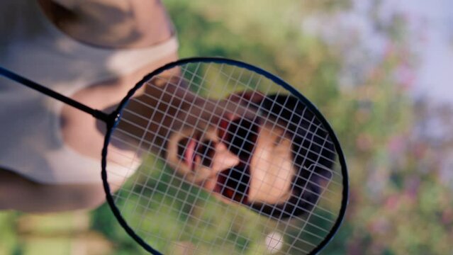 outdoors in a park with trees young brunette boy standing with a bambinton racket trying to tighten the strings on the racket