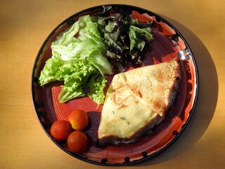 Plate with a pancake accompanied by green salad and cherry tomatoes.