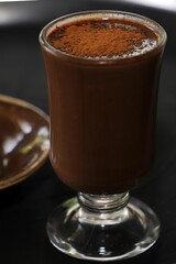 Close-up of a glass filled with rich, creamy chocolate drink topped with cocoa powder