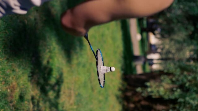 vertical video close up outdoors in a park with trees young handsome brunette guy in jeans and a white T-shirt, a brunette stuffing a shuttlecock warming up before playing bambinton