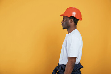 Standing and posing, construction worker in hard hat. Handsome black man is in the studio against...