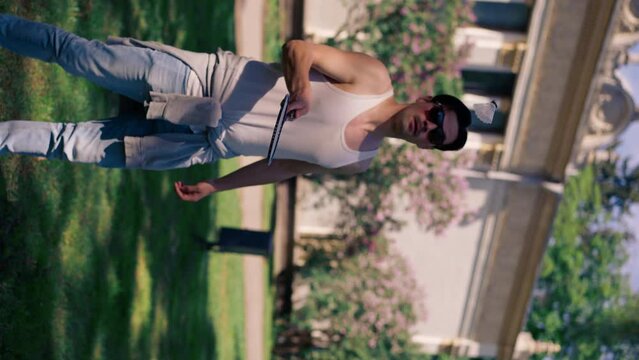 vertical video outdoors in a park with trees young handsome brunette guy in jeans and a white T-shirt, a brunette stuffing a shuttlecock warming up before playing bambinton