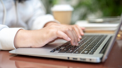 A close-up image of a woman working on her laptop computer, typing on the laptop keyboard.