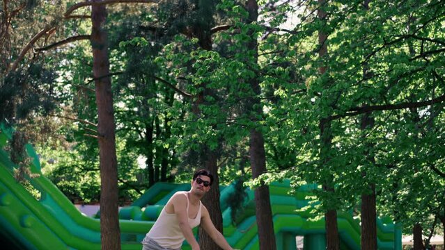 outdoors in a park with trees young handsome brunette guy in jeans and a white T-shirt, a brunette stuffing a shuttlecock warming up before playing bambinton