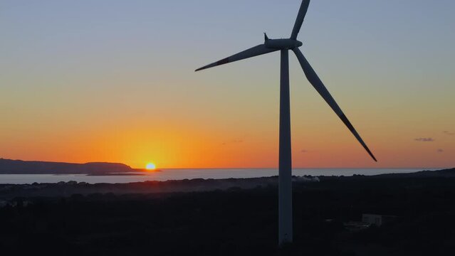 Wind turbine spinning at sunset on the coastline. The sun and the sea in the background. Silhouette