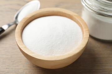 Baking soda in bowl on wooden table, closeup