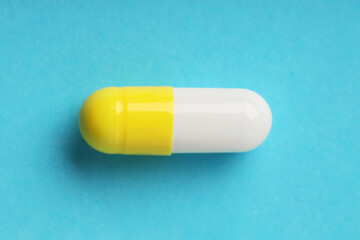 One antibiotic pill on light blue background, top view. Medicinal treatment