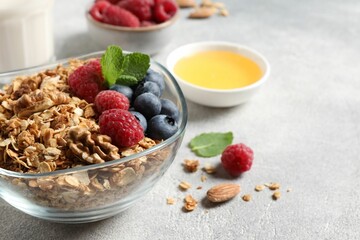Tasty granola with berries, nuts and mint on grey table, closeup. Space for text