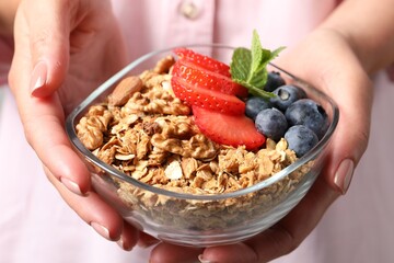 Woman holding bowl of tasty granola with berries, nuts and mint, closeup