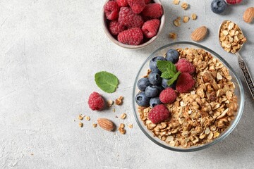 Tasty granola with berries, nuts and mint on grey table, flat lay. Space for text