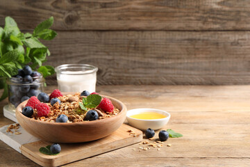 Tasty granola with berries, nuts and mint on wooden table, space for text