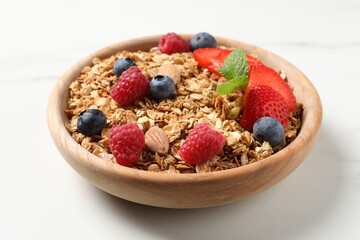 Tasty granola with berries, nuts and mint on white table