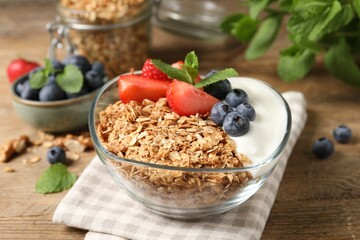 Tasty granola with berries and yogurt in bowl on wooden table, closeup