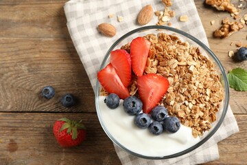 Tasty granola with berries and yogurt in bowl on wooden table, flat lay
