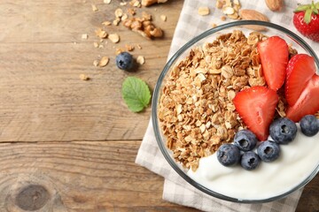 Tasty granola with berries and yogurt in bowl on wooden table, flat lay. Space for text