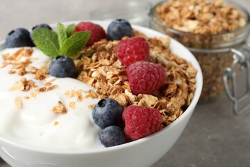 Tasty granola with berries and yogurt in bowl on grey textured table, closeup