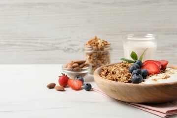 Tasty granola with berries and yogurt in bowl on white marble table, closeup. Space for text