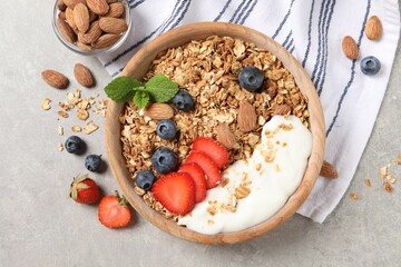 Tasty granola with berries, almond and yogurt in bowl on grey textured table, flat lay