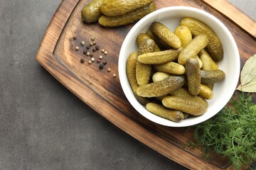 Pickled cucumbers in bowl, dill and peppercorns on grey textured table, top view
