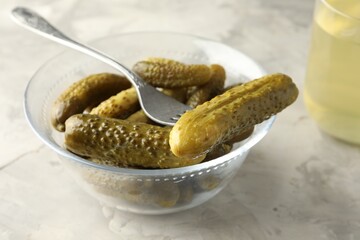 Pickled cucumbers in bowl and fork on grey textured table, closeup