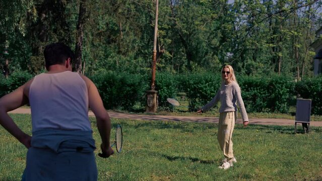 outdoors in a park with trees a young brunette guy with a blonde girl playing bambinton best friends relaxing together the girl serves