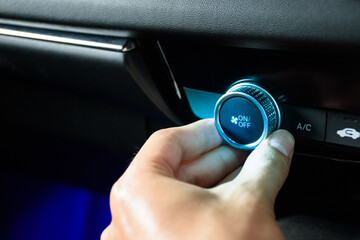 Hand turning the button car air conditioning fan to air condition the interior of a modern luxurious car with blue light in 2024.