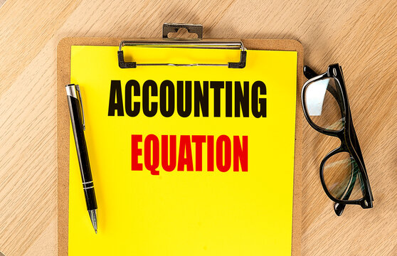 ACCOUNTING EQUATION text on yellow paper on clipboard with pen and glasses