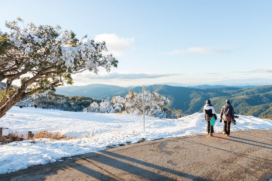 Mount Buller in Victoria, Australia. A pair of snowboarders walk across the snow to admire the view of the mountains.