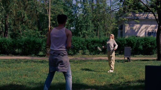 outdoors in a park with trees a young brunette guy with a blonde girl playing bambinton best friends relaxing together the girl serves
