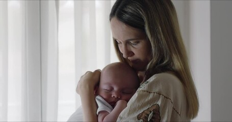 Super slow motion of young happy mother caressing with affection her newborn baby boy while sleeping in her arms in a nursery. Parenthood, childcare, life, maternity, motherhood - Powered by Adobe