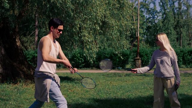 on the street in the park among the trees young brunette guy with a blonde is juggling rackets for playing bambinton