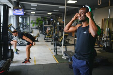 Athletic man standing in a gym listening to music using wireless headphones