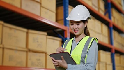 Young female worker in uniform checklist manage parcel box product in logistic warehouse.Asian woman employee holding tablet working at store industry.Logistic import export business concept