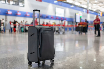 A gray luggage suitcase standing on the floor at a crowded airport terminal. Blurry people on the background.