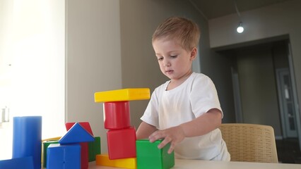 boy kid playing toy in kindergarten. happy family kid dream education concept. baby son plays toys colored cubes on lifestyle the table in kindergarten indoors. blond boy 2 years playing toys