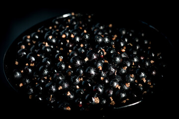 Black currants in a plate on a black background. Berries concept