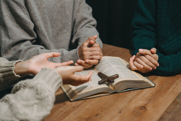 Group of Christians sit together and pray around a wooden table with blurred open Bible pages in...