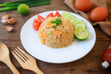 Egg fried rice with lime , tomato and cucumber on a white plate, wooden blackground , thai food