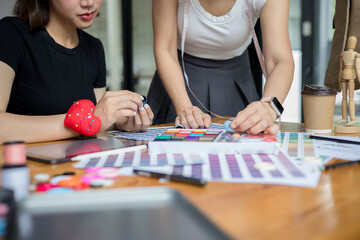 Fototapeta premium Two designer are working at a table with a color swatch chart and making notes. collaborative design or fashion project and creativity