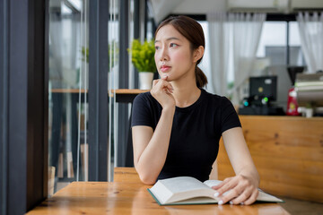 Young asian woman is sitting and reading a book at a cafe