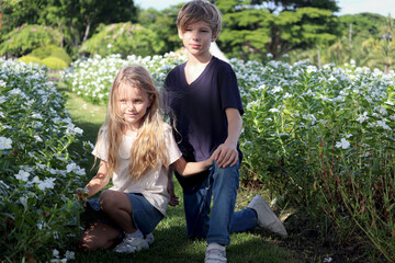 Happy family, brother and sister playing at beautiful flower garden. Joyful kids, boy and girl have fun outdoor at public park. Children enjoy spending time outside. Sibling plays together.