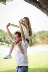 Father carrying cute daughter, joyful parent piggybacking his child girl at the park on summer holiday. Dad plays with kid and spends time outdoor together in beautiful garden. Happy family outside.