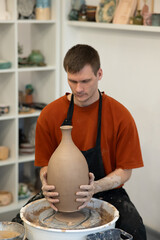A man makes a ceramic vase on a pottery wheel. Vertical photo. 