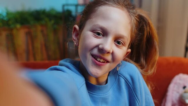 POV of child girl blogger taking selfie on smartphone, communicating video call online with social media subscribers. Female teenager kid recording video story at night home in room sits on couch